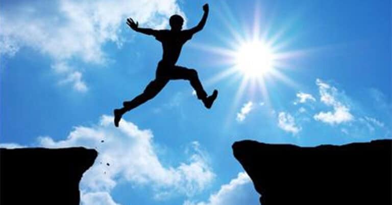 person jumping over chasm between cliffs